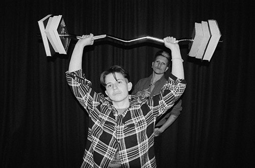 Marlo is lifting a barbell weighted with books with Silver looking on lustfully.